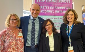 Four professionally dressed adults smile at the camera in front of a sign that reads “Stop losing nurses.” Dr. Cynthia Baker appears second from the right.